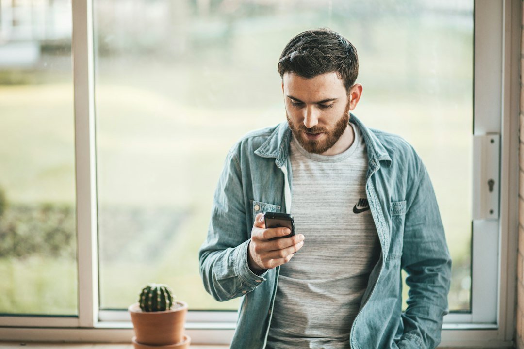 Adult looking thoughtfully at a phone by a window