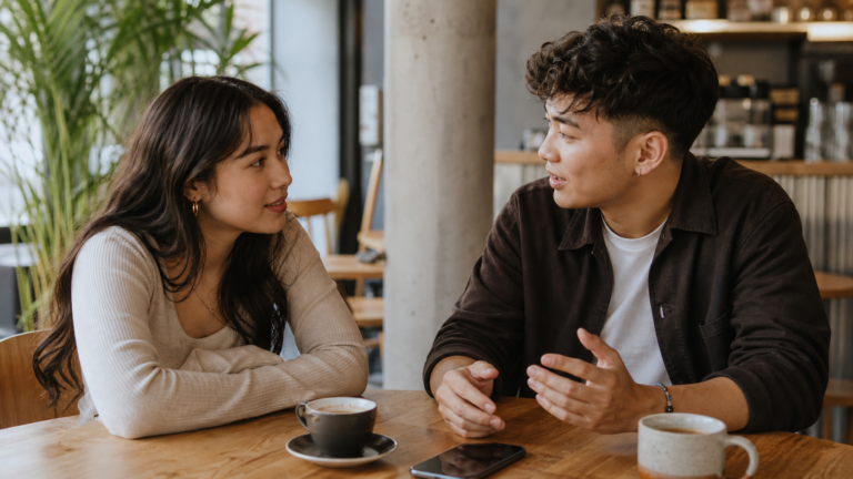 Two adults talking over coffee with a phone on the table, illustrating modern dating